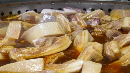 Pork ribs are being cooked on an industrial scale in large pans, simmering in a rich broth.