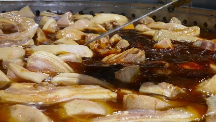Pork ribs are being cooked on an industrial scale in large pans, simmering in a rich broth.