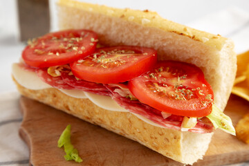 Homemade Italian Sub Sandwich with Salami, Tomatoes and Shredded Iceberg Lettuce on a rustic wooden board, side view.