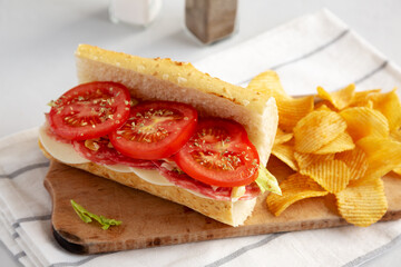 Homemade Italian Sub Sandwich with Salami, Tomatoes and Shredded Iceberg Lettuce on a rustic wooden board, side view.