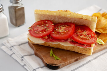 Homemade Italian Sub Sandwich with Salami, Tomatoes and Shredded Iceberg Lettuce on a rustic wooden board, side view.