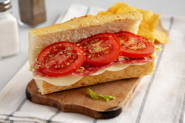 Homemade Italian Sub Sandwich with Salami, Tomatoes and Shredded Iceberg Lettuce on a rustic wooden board, side view.