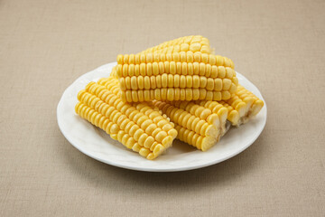 Raw corn kernels and cobs sliced on white plate
