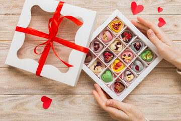 Female hands with delicious candies in box on color background