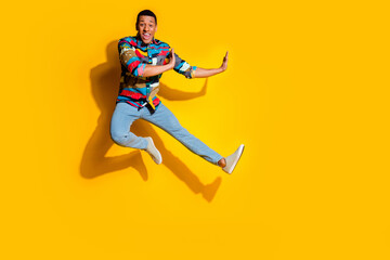 Full length photo of nice young male jump kicking dressed stylish colorful garment isolated on yellow color background