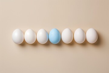 Eggs lineup with one blue among white, against light beige backdrop, idea of gender diversity