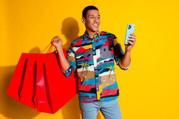 Photo portrait of nice young male shopping bags hold device dressed stylish colorful garment isolated on yellow color background