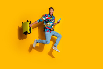 Full length photo of nice young male suitcase hold device running dressed stylish colorful garment isolated on yellow color background