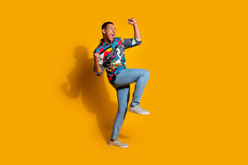 Full size photo of handsome young guy winning raise fists wear trendy colorful outfit isolated on yellow color background
