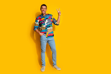 Fototapeta premium Full size photo of handsome young guy show v-sign wear trendy colorful outfit isolated on yellow color background