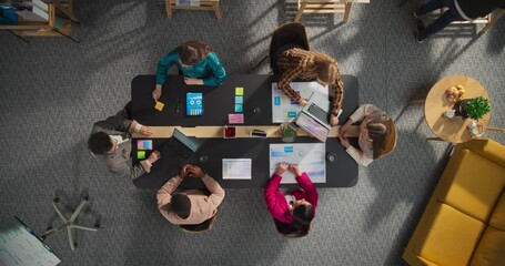 Top Down Zoom Out Shot: Diverse Team Collaborates on Digital Marketing Strategies. Businesspeople Analyze Data, Discuss Ideas and Use Laptops in Office. Creative Workspace With Charts and Infographics