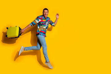 Full body photo of attractive young man suitcase wave hand running dressed stylish colorful clothes isolated on yellow color background
