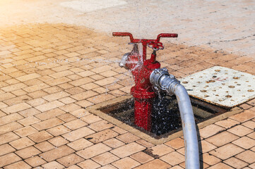 red fire hydrant with connected hose with splashing water for firefighting on the sidewalk outside...