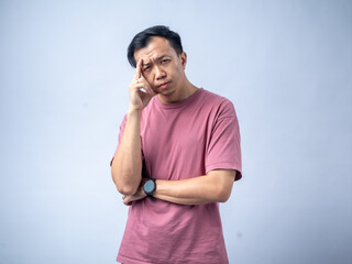 A man in a pink shirt looks thoughtfully upwards with his hand on his chin, reflecting a pensive...