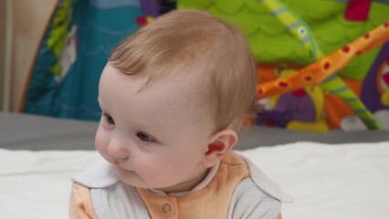 Adorable happy blonde infant baby playing with kids toys at home while sitting on carpet floor in living room. Portrait of smiling cute child toddler using colorful toys, copy space