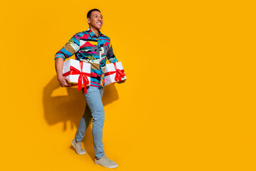 Fototapeta premium Full body photo of attractive young man carry gifts walk dressed stylish colorful clothes isolated on yellow color background