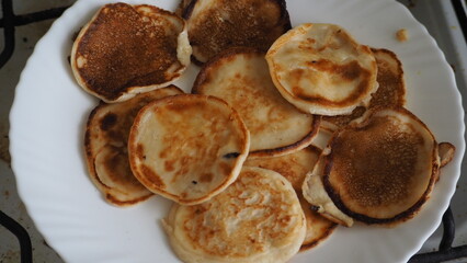 Housewife woman bakes pancakes for breakfast and pours dough into hot frying pan. Homemade pancakeson glass-ceramic stove in kitchen. Ingredients for making pancakes. Selective focus.