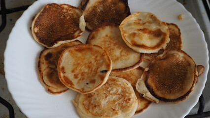 Housewife woman bakes pancakes for breakfast and pours dough into hot frying pan. Homemade pancakeson glass-ceramic stove in kitchen. Ingredients for making pancakes. Selective focus.