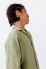 Stylish young boy in olive green shirt with braids in hair gazes off into the distance