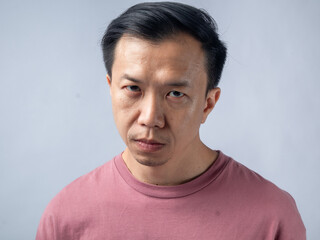 Obraz premium A serious man in a pink shirt gazes intensely at the camera, showing a stern expression. The plain light blue backdrop emphasizes his focused and contemplative demeanor.