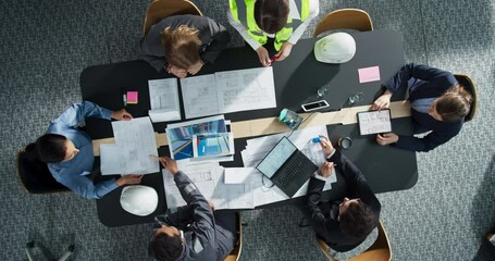 Top Down View of Diverse Team of Business Professionals and Engineers Working Together on Architectural Plans in a Corporate Office. Focused Colleagues Using Laptop, Tablet, Blueprints And Documents.