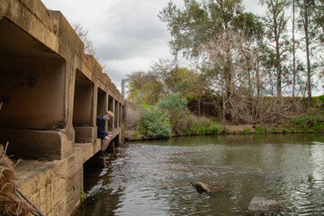 Naklejka premium Teen boy sitting under low bridge over the Cudgegong River in rural New South Wales