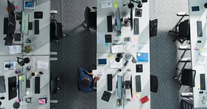 Top Down View Of Male African American Worker Staying Late At Work Alone In A Corporate Office. Black Man Using Desktop Computer To Analyze Financial Data, Create Reports For Senior Management.