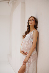 Beautiful pregnant woman in white retro underwear lace dress and white sandals with high heels. Big pregnant belly. Pretty woman waiting child. Light play on woman's body and face