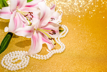 White lilies and pearl necklace on a shiny gold background
