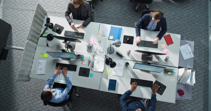 Top Down View of Diverse Team in a Corporate Office, Working on Desktop Computers And With Financial Documents. Colleagues Working Creating Reports, Developing Business Strategies For Hedge Fund.