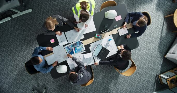 Top Down View of Diverse Team of Real Estate Construction Engineers Working With Blueprints and Documents in an Office. Workspace Of Housing Development Company With Colleagues Using Laptop And Tablet