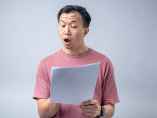 A man in a pink shirt looks excitedly at a stack of papers he is holding, his mouth open in...