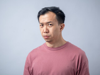 Obraz premium An Asian man in a pink shirt makes a skeptical and uncomfortable expression, as if reacting to something unpleasant. The plain light blue background highlights his displeased