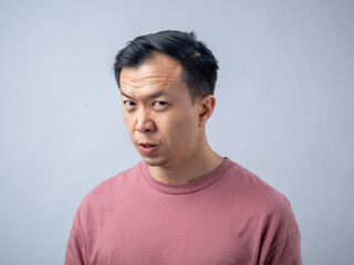 An Asian man in a pink shirt makes a skeptical and uncomfortable expression, as if reacting to...