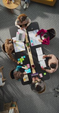 Vertical Screen Top Down View: Innovative Teamwork at Office Table. Diverse Professionals Collaborate Using Laptops and Tablets, Strategizing and Brainstorming For Creative Business Problem Solving