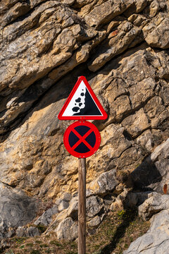 A classic falling rocks warning sign is pictured with a backdrop of a rugged rocky cliff face, providing a clear and urgent reminder of potential hazards in the area.