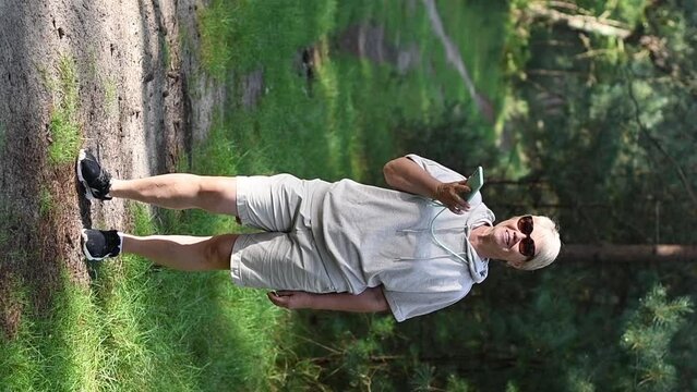 woman in the forest in beige knitted suit takes her daily steps, breathes the air of a pine forest, records an audio message on a smartphone, blogs on social networks, 5G internet,Slow motion