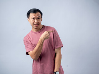 An Asian man in a pink shirt points to his side with a surprised and curious expression, as if...
