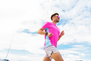 Man in bright pink athletic wear and sunglasses runs under a clear, sunny sky, exuding energy and joy.