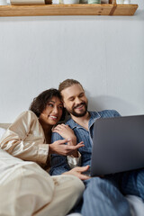 A loving couple cuddles on the couch while watching a movie on their laptop.