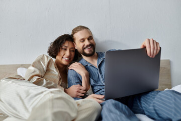 A loving couple is seen relaxing together at home, cuddling and watching something on a laptop.