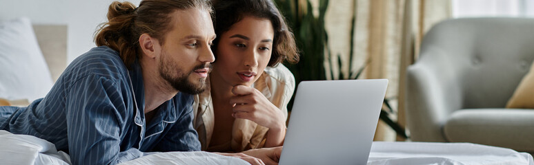 A loving couple cuddles in bed while looking at a laptop.