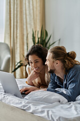 A loving couple spends time together at home, relaxing in bed and browsing the internet on a laptop.