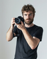 Man with tousled brown hair and a beard is holding a camera looking directly at the viewer photography