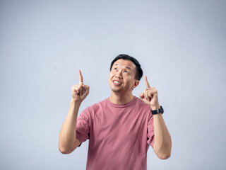 A man in a pink shirt points upwards with both index fingers and an enthusiastic expression, as if presenting an idea or emphasizing a point. The plain light blue background highlights his animated