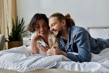 A couple relaxes in bed, sharing a laugh and a phone.