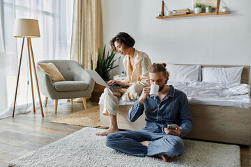 A couple enjoys a relaxed morning at home, one working on a laptop, the other sipping coffee.