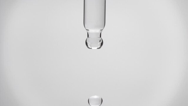 Cosmetics transparent liquid dripping from laboratory glass pipette in super slow motion. Macro shot of drop hanging down from chemical dropper. Abstract body care serum ingredients concept