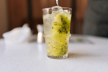 Closeup of unrecognizable bartender pouring fresh alcoholic drink to glass with kiwi and ice cubes to make deliciously refreshing cocktail. Concept of party time, holidays, celebration mood.