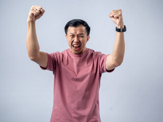 A man in a pink shirt raises both fists in a celebratory gesture, his face beaming with excitement...